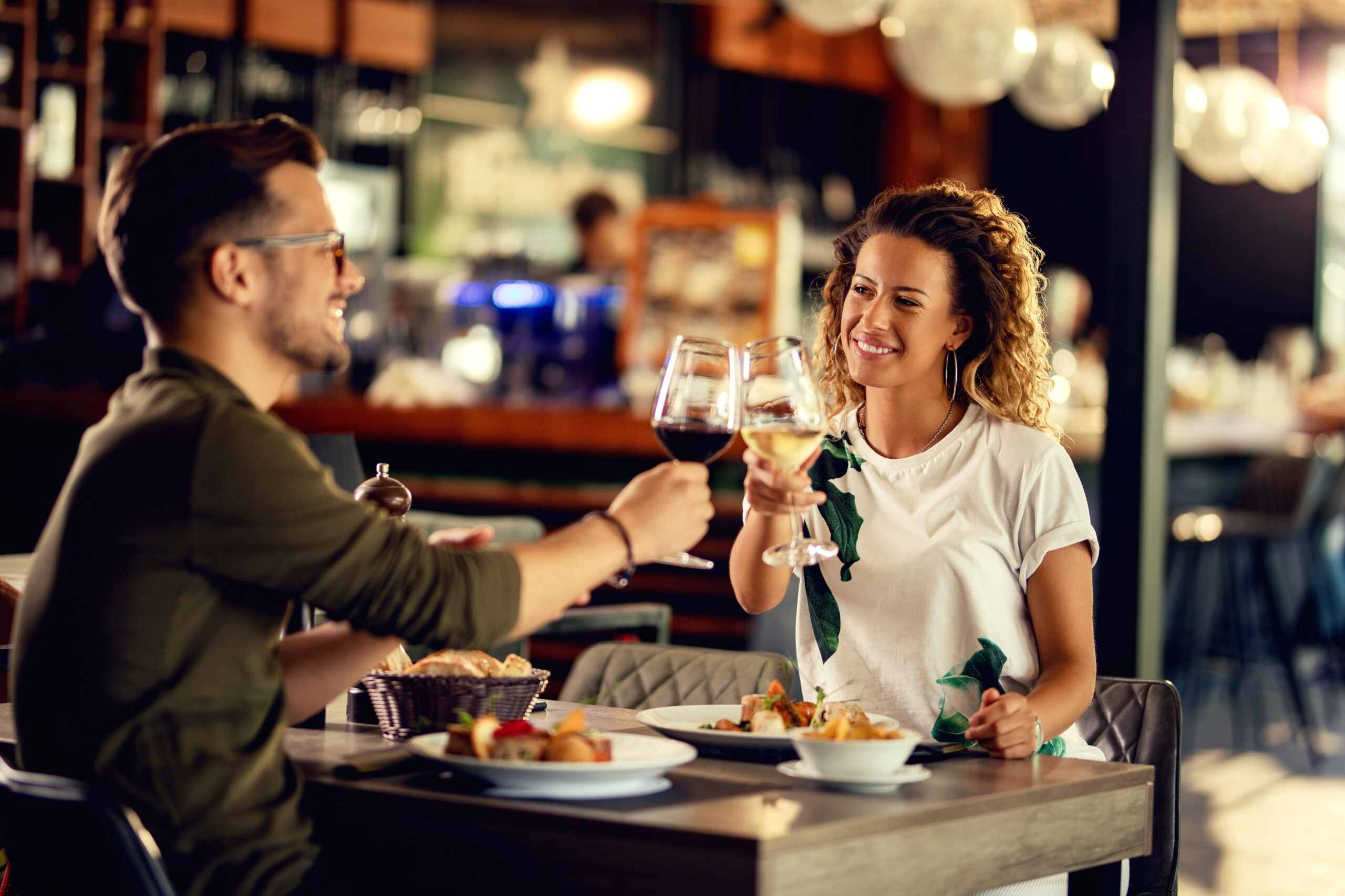 Young happy couple celebrating and toasting with wineglasses while eating in a restaurant.